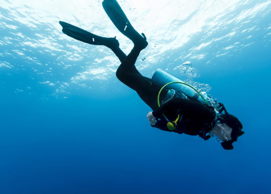 An underwater photograph of a scuba diver. Their head is pointed down and a steady stream of bubbles rises from their mouth towards the surface (Credit: www.visithowth.ie)